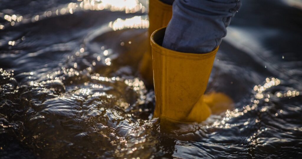 Pessoa de botas amarelas dentro da água, representando o risco de enchente que o Fundo Gaúcho de Riscos Climáticos quer cobrir